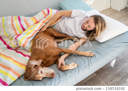 Relaxed woman spending comfy weekend morning time lying in cozy bed with beloved Vizsla dog. Relaxed woman spending comfy weekend morning time lying in cozy bed with beloved Vizsla dog. 138538192
