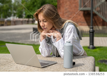 Curious positive businesswoman works on laptop outdoors, focused lady watching webinar on computer. Curious positive businesswoman works on laptop outdoors, focused lady watching webinar on computer. 138538253