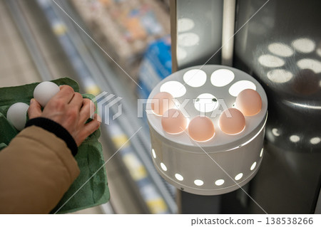 Unrecognizable female customer in shop checking raw eggs contents in ovoscope candling station. Unrecognizable female customer in shop checking raw eggs contents in ovoscope candling station. 138538266