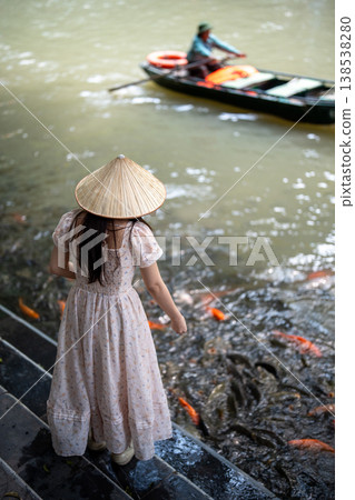 Woman feeding colorful koi carps in pond, positive relaxing leisure activity for tourists in Vietnam Woman feeding colorful koi carps in pond, positive relaxing leisure activity for tourists in Vietnam 138538280
