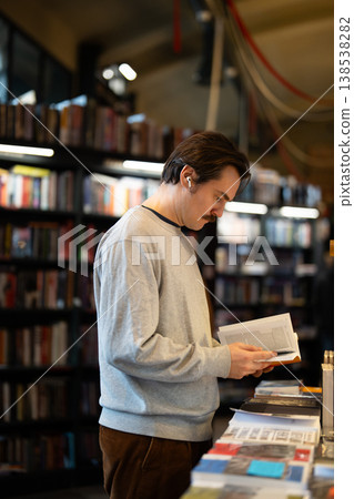 Focused smart man reviewing textbook in trendy bookshop, inspecting through content of popular novel 138538282