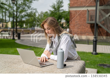 Focused positive businesswoman working on laptop outdoors, enjoying remote work on fresh air. 138538345