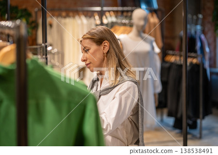 Positive woman customer choosing clothes in fashion shop, lady client mindfully examinees assortment 138538491