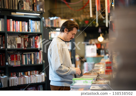 Relaxed thoughtful man booklover reading titles and picking books from display in local bookshop. 138538502