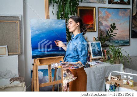 Positive woman artist painting on canvas at cozy loft apartment, full of ideas and inspiration. 138538508
