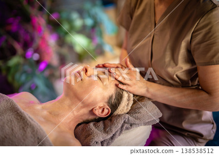 Dreamy woman receiving healing relaxing facial massage treatment with aromatic oils in beauty clinic Dreamy woman receiving healing relaxing facial massage treatment with aromatic oils in beauty clinic 138538512