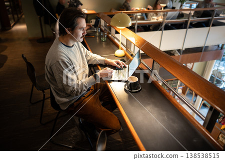 Positive relaxed businessman working on remote using laptop in trendy co-working cafe space. Positive relaxed businessman working on remote using laptop in trendy co-working cafe space. 138538515