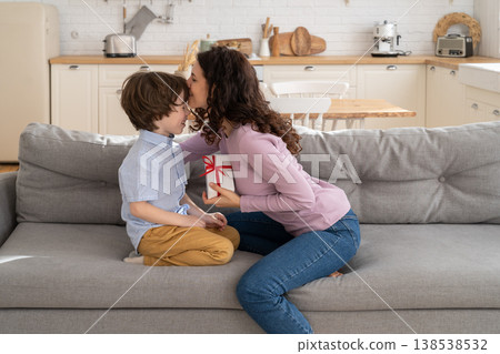 Mom kissing child, receives wrapped gift box with red bow from son for her birthday. Loving family. Mom kissing child, receives wrapped gift box with red bow from son for her birthday. Loving family. 138538532