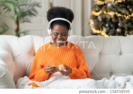 Cozy xmas or new year morning at home: happy young african woman listen music eat tangerines in bed Cozy xmas or new year morning at home: happy young african woman listen music eat tangerines in bed 138538545
