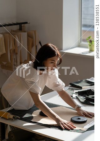 Young designer female put pattern on fabric to cut template. Dressmaker work with textile in atelier Young designer female put pattern on fabric to cut template. Dressmaker work with textile in atelier 138538551