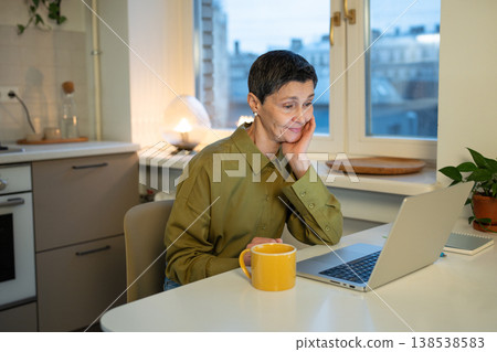 Happy thoughtful senior businesswoman looking at laptop screen with positive smiling expression. Happy thoughtful senior businesswoman looking at laptop screen with positive smiling expression. 138538583