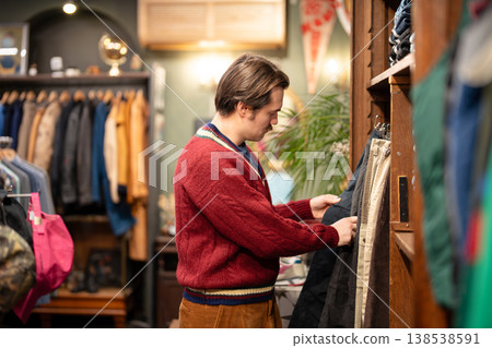 Attractive man in knit sweater on shopping day in vintage clothing store, buying second hand pants. Attractive man in knit sweater on shopping day in vintage clothing store, buying second hand pants. 138538591