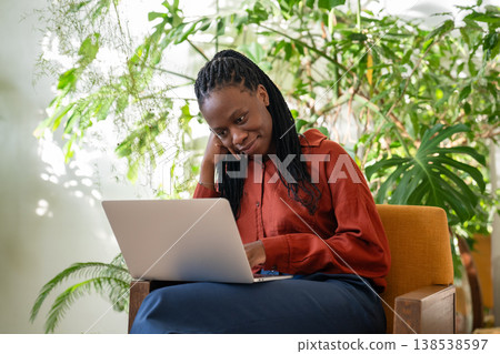 Relaxed smiling African American businesswoman works on laptop in cozy home green tropical garden. 138538597