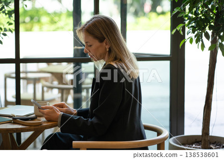 Relaxed businesswoman using smartphone while sitting at cafe table on lunch break from work. 138538601