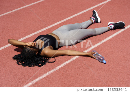 Powerless African American woman in sportswear lies on red track covering eyes with hand from sun Powerless African American woman in sportswear lies on red track covering eyes with hand from sun 138538641