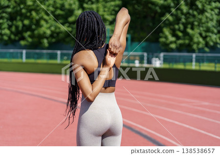 African American woman stretches hands and back standing on red track of big stadium near park African American woman stretches hands and back standing on red track of big stadium near park 138538657