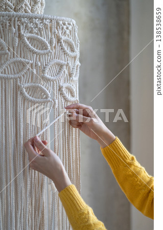Close up of woman working on half-finished macrame piece, weaves lamp shade for chandelier. Hobby. Close up of woman working on half-finished macrame piece, weaves lamp shade for chandelier. Hobby. 138538659