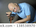 A bearded old man is doing rehabilitation indoors using a cane. 138538970