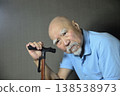 A bearded old man is doing rehabilitation indoors using a cane. 138538973