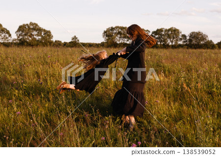 Caucasian Woman And Daughter Involved In Lively Spinning Game In Open Field At Dusk Caucasian Woman And Daughter Involved In Lively Spinning Game In Open Field At Dusk 138539052