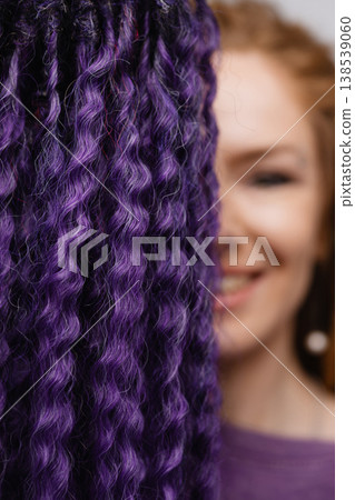 Smiling woman with dreadlocks partially hidden behind purple hair strands Smiling woman with dreadlocks partially hidden behind purple hair strands 138539060