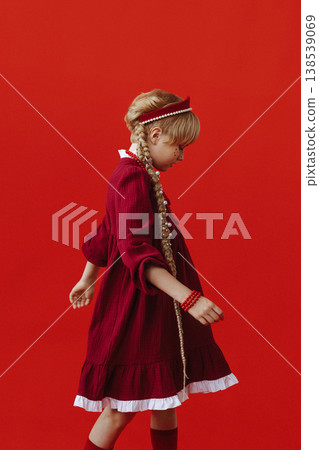 Caucasian girl in red folk dress with braids standing on red background Caucasian girl in red folk dress with braids standing on red background 138539069