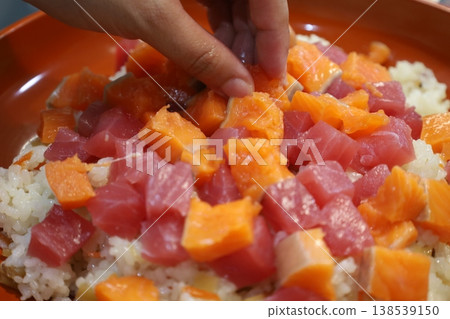 特寫鏡頭:雙手將鮪魚和鮭魚放在散壽司上。 特寫鏡頭:雙手將鮪魚和鮭魚放在散壽司上。 138539150