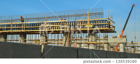 Large concrete road bridge construction site with formwork, rebar, workers, and a mobile crane working on new infrastructure development under a clear blue sky. Large concrete road bridge construction site with formwork, rebar, workers, and a mobile crane working on new infrastructure development under a clear blue sky. 138539180
