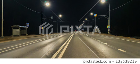 Empty asphalt highway at night illuminated by rows of streetlights, passing a bus stop and pedestrian crosswalks under a dark sky, tranquil and deserted urban scene. Empty asphalt highway at night illuminated by rows of streetlights, passing a bus stop and pedestrian crosswalks under a dark sky, tranquil and deserted urban scene. 138539219