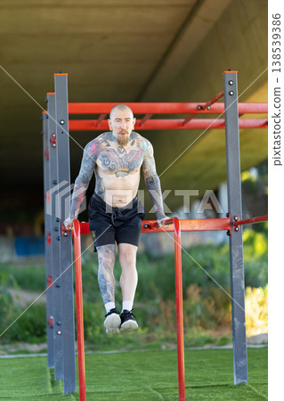 Tattooed man performing calisthenics workout on parallel bars Tattooed man performing calisthenics workout on parallel bars 138539386