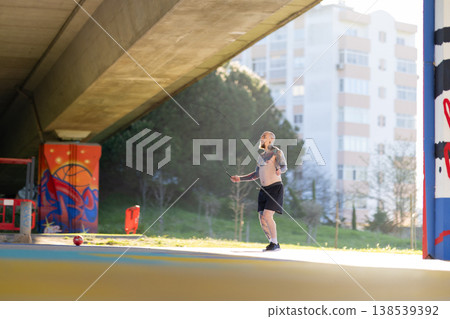 Tattooed man skipping rope under urban bridge Tattooed man skipping rope under urban bridge 138539392