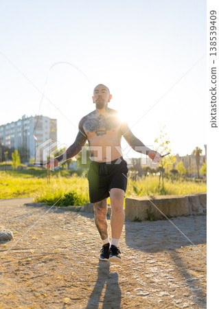 Tattooed man skipping rope performing outdoor workout 138539409