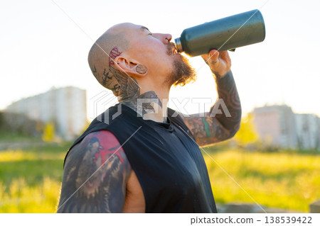 Tattooed man drinking water after workout 138539422