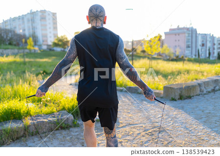 Tattooed man exercising jump rope in urban park Tattooed man exercising jump rope in urban park 138539423