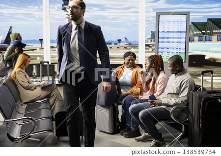 Joyful African American family with teenager sitting in airport lounge before boarding plane, luggage and air travel bags. Parents and daughter shares bonding moment in good mood. 138539734