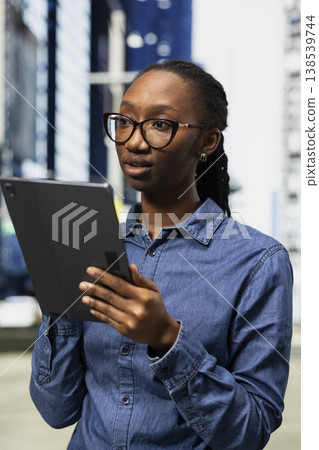 Freelance artist outside using device tactile touchscreen to draw, finishing project for client. African american woman doing digital art on drawing tablet in city metropolitan area 138539744
