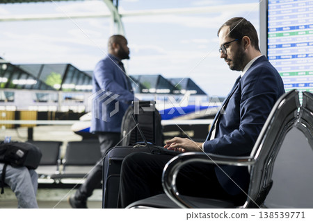 Man entrepreneur preparing for business trip in busy airport terminal lounge, ready for boarding plane and flight departure. Business traveler frequent flyer with tablet and luggage. 138539771
