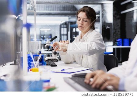 Scientist in high tech laboratory checking time while doing genetics study using lab equipment. Woman using scientific gear in research facility waiting for complex experiment to finish Scientist in high tech laboratory checking time while doing genetics study using lab equipment. Woman using scientific gear in research facility waiting for complex experiment to finish 138539775
