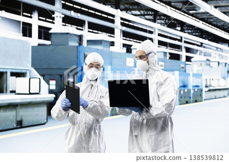 Team of technicians in PCB factory cleanroom monitoring production lines equipment telemetry. Teamworking colleagues wearing safety gear using devices to document microchip yield variations Team of technicians in PCB factory cleanroom monitoring production lines equipment telemetry. Teamworking colleagues wearing safety gear using devices to document microchip yield variations 138539812