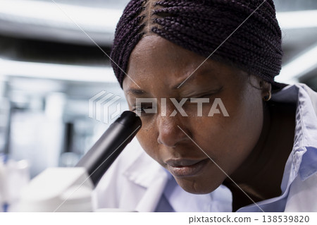 Close up of african american expert uses microscope with glass tray of samples as observation tool. Experiment combines molecular biology for genetics research and investigation. 138539820
