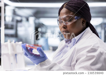 Researcher inspects Petri dish with magnifying glass during lab experiment. Cellular investigation and molecular biology analysis support genetics research and advanced medical science. 138539840