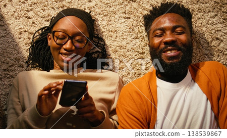 Top down view of black couple laying on the floor and enjoying free time, positive ambience with relaxation and laughter. Two people spending quality time together, serene domestic life. Top down view of black couple laying on the floor and enjoying free time, positive ambience with relaxation and laughter. Two people spending quality time together, serene domestic life. 138539867