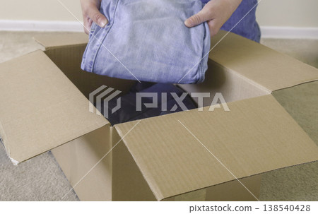 Packing clothes into cardboard box at home Packing clothes into cardboard box at home 138540428