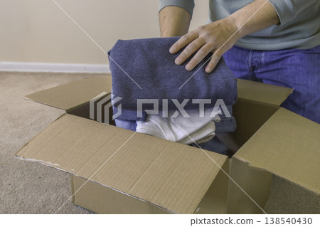 Packing clothes into cardboard box at home Packing clothes into cardboard box at home 138540430
