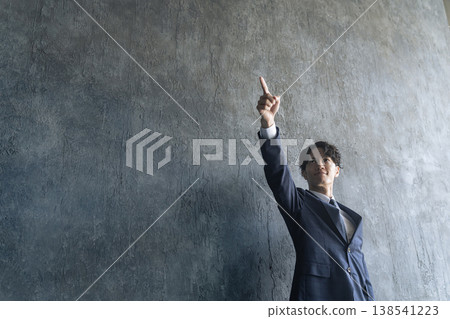 A young male businessperson points upwards. A young male businessperson points upwards. 138541223