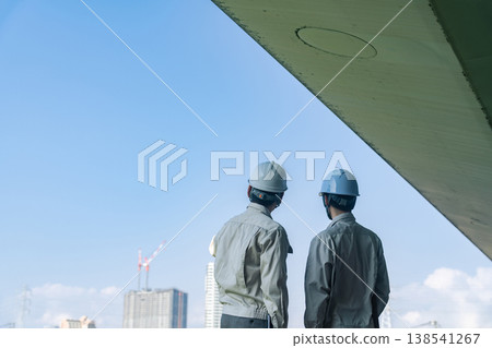 A group of male workers looking out at a city under construction. A group of male workers looking out at a city under construction. 138541267