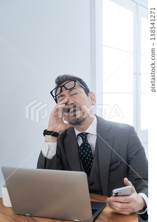 一位中年男性商務人士在使用智慧型手機和筆記型電腦時遇到問題,正在努力解決。 一位中年男性商務人士在使用智慧型手機和筆記型電腦時遇到問題,正在努力解決。 138541271