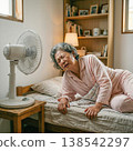 A senior woman appears uncomfortable sleeping in a room with a fan. 138542297