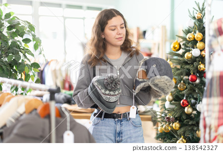 Young girl choosing winter hat in clothing store during Christmas Young girl choosing winter hat in clothing store during Christmas 138542327