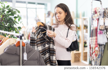 Woman holding a hanger with outerwear in her hands in a store Woman holding a hanger with outerwear in her hands in a store 138542376